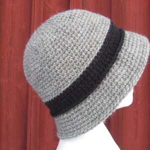 May include: A gray crocheted hat with a wide black band around the crown. The hat is shown from the side.