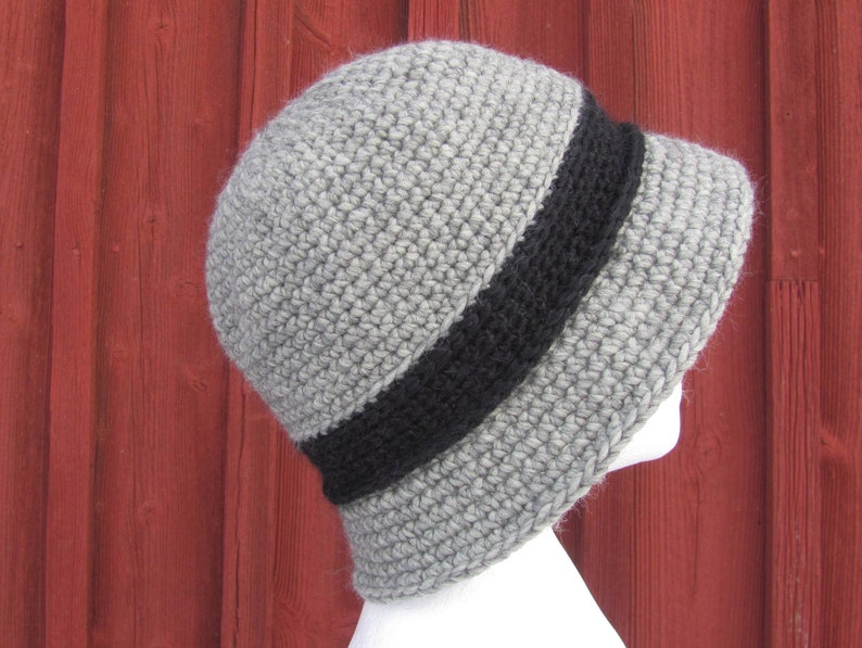 May include: A gray crocheted hat with a wide black band around the crown. The hat is shown from the side.