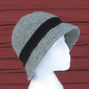 May include: A gray crocheted hat with a black stripe around the crown. The hat is on a white mannequin head.