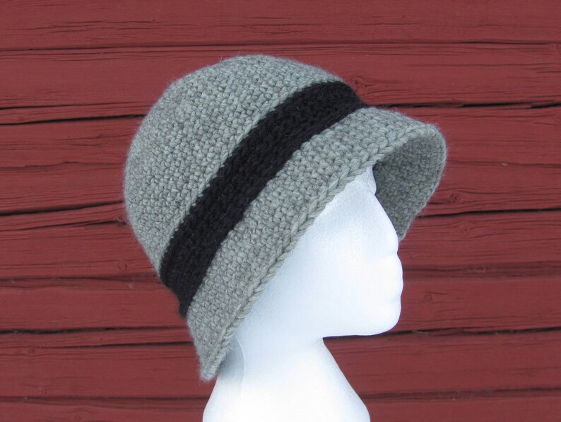 May include: A gray crocheted hat with a black stripe around the crown. The hat is on a white mannequin head.