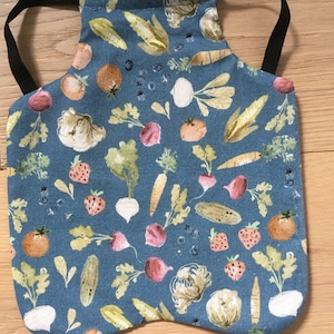 May include: A blue fabric apron with a pattern of colorful vegetables and strawberries. The apron has adjustable black elastic straps.