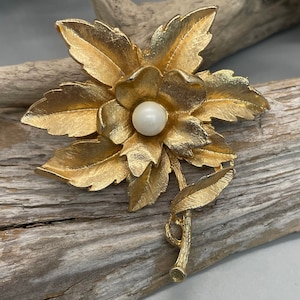 Vintage 1970s gold tone flower brooch with faux pearl center.