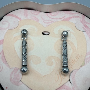 May include: A white ceramic mug with a black handle and the text "But First, Coffee" in a bold, black font. The mug is set against a blurred background, suggesting a cozy setting.