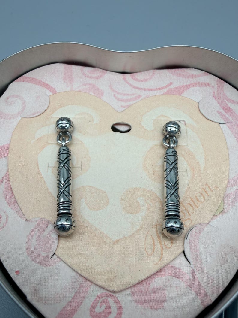 May include: A white ceramic mug with a black handle and the text "But First, Coffee" in a bold, black font. The mug is set against a blurred background, suggesting a cozy setting.