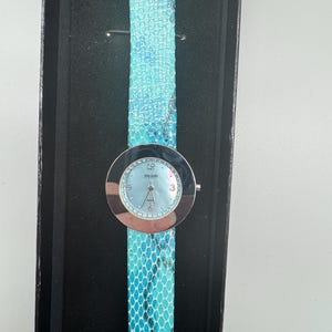 May include: A silver watch with a blue face and a blue snakeskin band. The watch is in a black box.