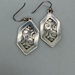 Puede incluir: Un par de pendientes plateados. Cada pendiente presenta un marco geom&eacute;trico hexagonal con un dise&ntilde;o calado de espirales. Los pendientes tienen un cierre de gancho y una peque&ntilde;a cuenta dorada cerca de la parte superior.