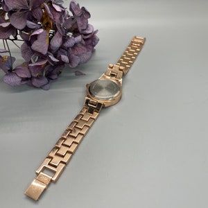 May include: A gold-tone watch with a metal band. The watch face is round and has a silver-tone finish.