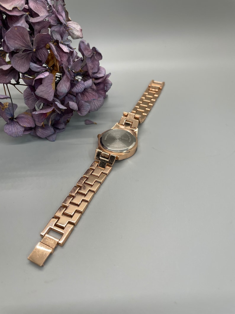 May include: A gold-tone watch with a metal band. The watch face is round and has a silver-tone finish.
