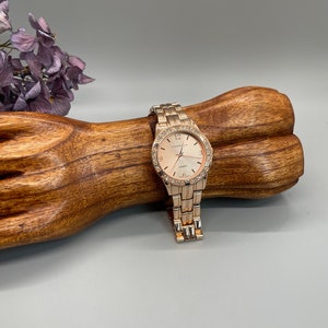 May include: A gold-tone watch with a white face and a crystal-encrusted bezel. The watch is on a gold-tone metal band.