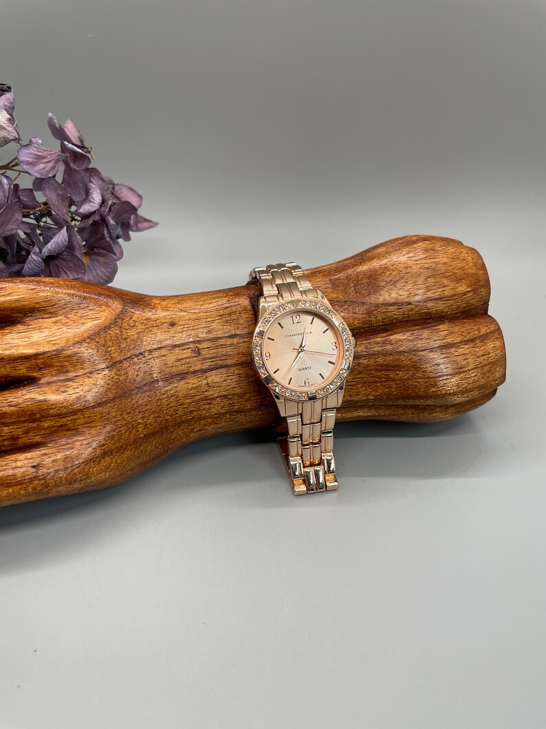 May include: A gold-tone watch with a white face and a crystal-encrusted bezel. The watch is on a gold-tone metal band.