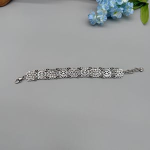 以下が含まれることがあります： 黒いハンドルと「But First, Coffee」のテキストが黒い太字で書かれた白いセラミックマグ。マグは白い表面に置かれています。