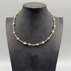 May include: A necklace featuring a silver-toned twisted cable chain interspersed with small, round, gold-toned metal beads and several circular accents containing embedded multicolored stones set at regular intervals along the length of the chain.
