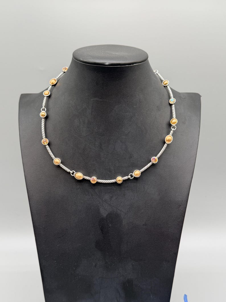 May include: A necklace featuring a silver-toned twisted cable chain interspersed with small, round, gold-toned metal beads and several circular accents containing embedded multicolored stones set at regular intervals along the length of the chain.