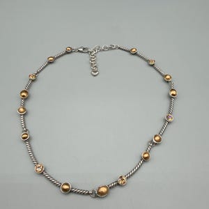 May include: A silver-toned necklace featuring a twisted cable chain design. The chain is accented with alternating round, metallic gold-toned beads and small, clear, faceted crystals set in silver-toned bezels. It includes a lobster claw clasp.