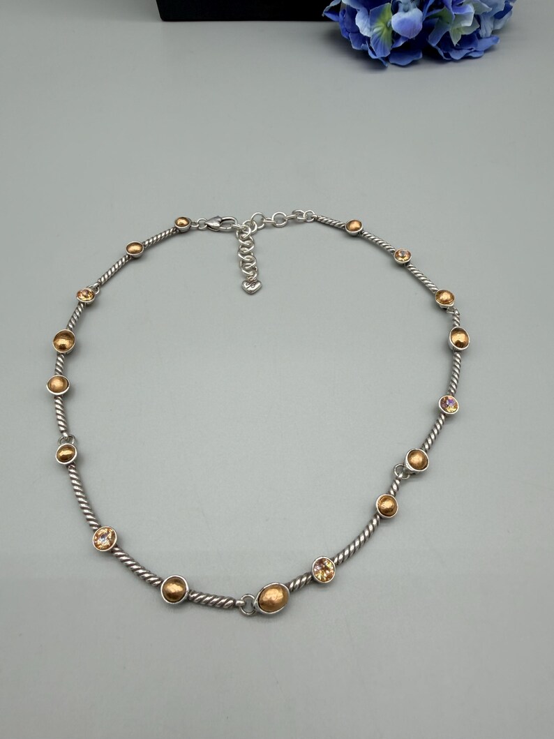 May include: A silver-toned necklace featuring a twisted cable chain design. The chain is accented with alternating round, metallic gold-toned beads and small, clear, faceted crystals set in silver-toned bezels. It includes a lobster claw clasp.