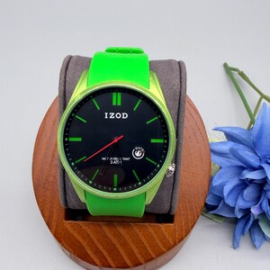 May include: An Izod wristwatch with a bright lime green silicone strap and a matching lime green bezel. The watch face is black with lime green hour markers, a red second hand, and a small date window. The text Izod is printed on the face.