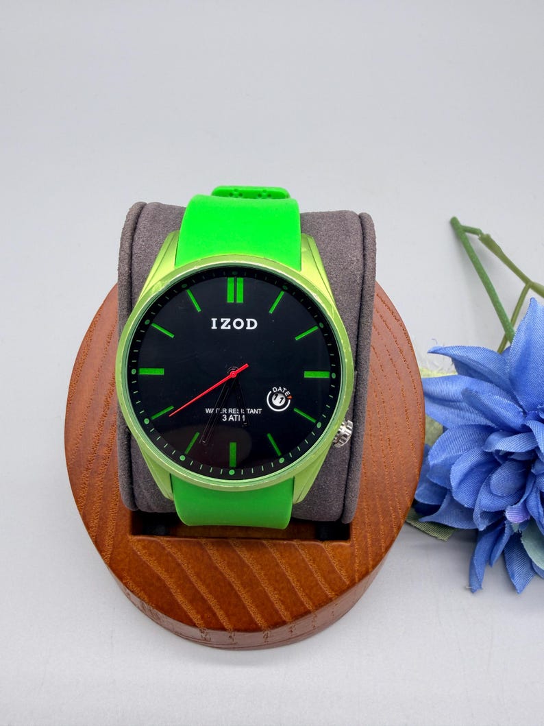 May include: An Izod wristwatch with a bright lime green silicone strap and a matching lime green bezel. The watch face is black with lime green hour markers, a red second hand, and a small date window. The text Izod is printed on the face.