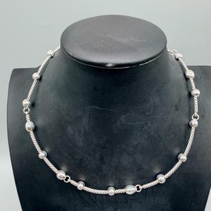 May include: A silver-toned necklace featuring a series of smooth, round metallic beads interspersed along a twisted, rope-textured chain. The design alternates between the polished spherical beads and segments of the twisted metal wire throughout.