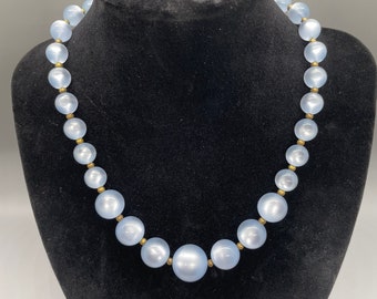 May include: A light blue glass bead necklace with gold accents. The necklace is on a black mannequin bust.