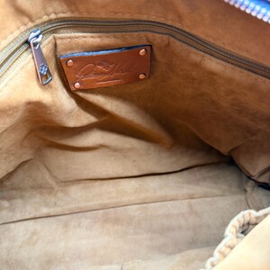 May include: Interior view of a brown leather handbag. The inside is lined with a soft, light brown material. A zipper runs along the top, and a leather tag with a logo is visible. The bag is open, showing the spacious interior.
