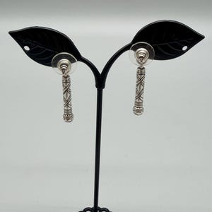 May include: A white ceramic mug with a black handle and the text "But First, Coffee" in a bold, black font. The mug is set against a blurred background, suggesting a cozy setting.