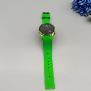 May include: A bright lime green wristwatch featuring a round black analog dial with the IZOD logo, thin green hour markers, and a matching lime green silicone strap with a silver-toned buckle and multiple adjustment holes for a secure fit.