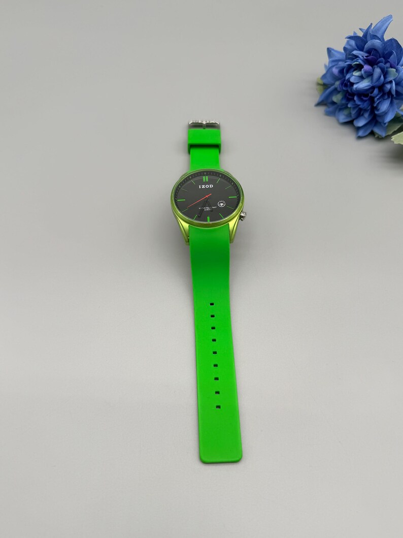 May include: A bright lime green wristwatch featuring a round black analog dial with the IZOD logo, thin green hour markers, and a matching lime green silicone strap with a silver-toned buckle and multiple adjustment holes for a secure fit.