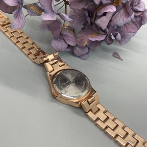 May include: A gold-tone wristwatch with a metal band. The watch face is silver and has the words "Charter Club" printed on it.