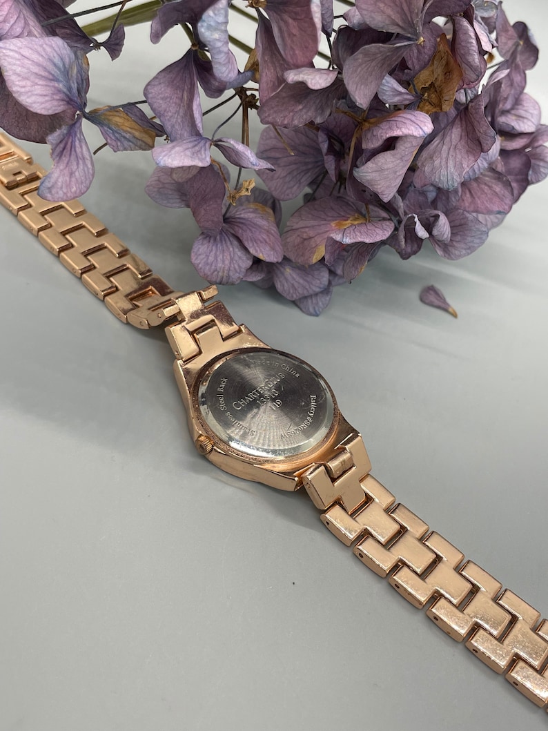 May include: A gold-tone wristwatch with a metal band. The watch face is silver and has the words "Charter Club" printed on it.