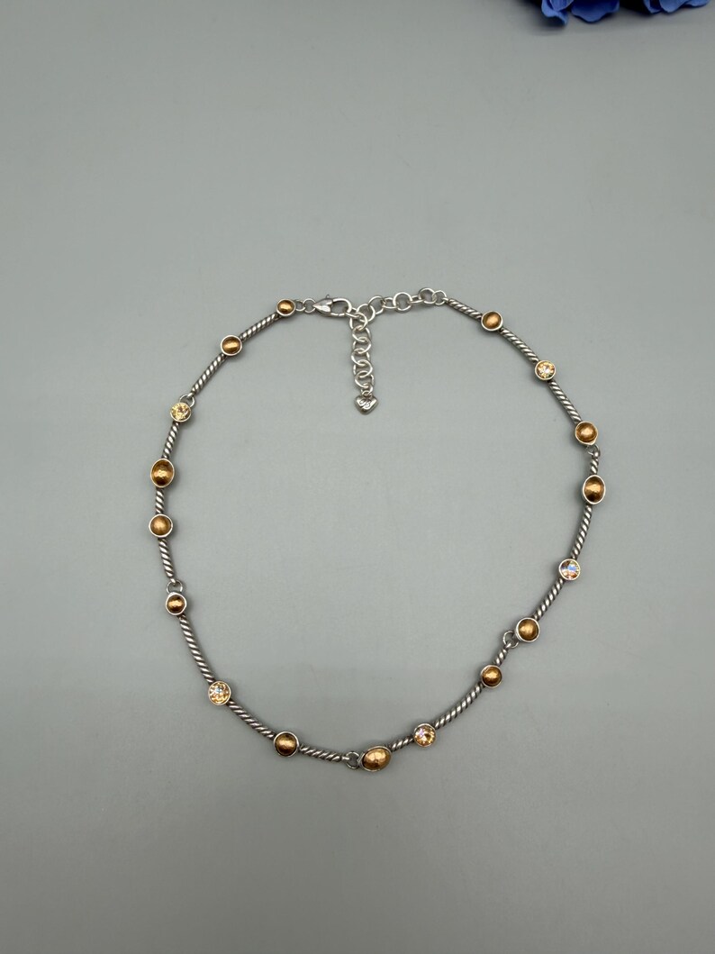May include: A silver-toned necklace featuring a twisted cable chain design. The chain is accented with alternating round, metallic gold-colored beads and small, clear, faceted crystals. It includes a lobster claw clasp and an adjustable chain extender.
