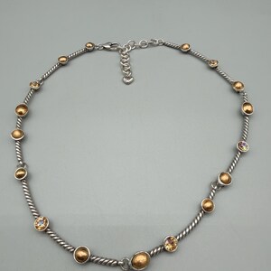 May include: A silver-toned necklace featuring a twisted cable chain design. The necklace is accented with alternating round, brushed gold-toned metal beads and small, faceted, light-reflecting crystals. It includes a lobster claw clasp and an extender chain.
