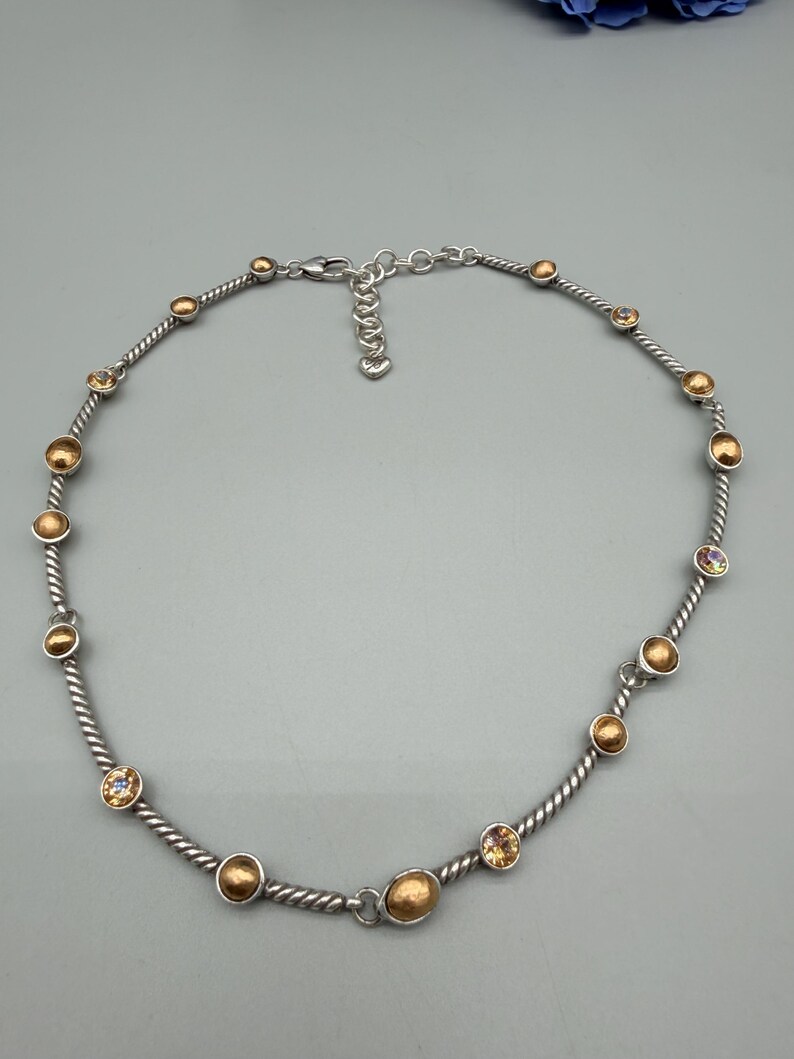 May include: A silver-toned necklace featuring a twisted cable chain design. The necklace is accented with alternating round, brushed gold-toned metal beads and small, faceted, light-reflecting crystals. It includes a lobster claw clasp and an extender chain.