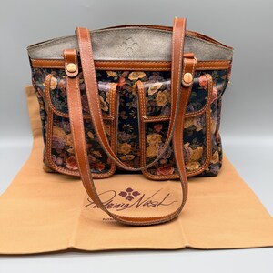 May include: A floral print tote bag with brown leather handles and accents. The bag features a dark background with colorful flowers and multiple exterior pockets. The brand name "Patricia Nash" is visible on the bag's dust cover.