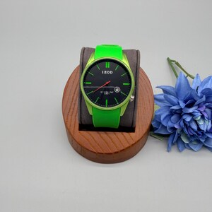 May include: An Izod wristwatch featuring a bright lime green silicone strap and matching lime green case. The watch face is black with lime green hour markers, a red second hand, and a small date window at the four o'clock position.
