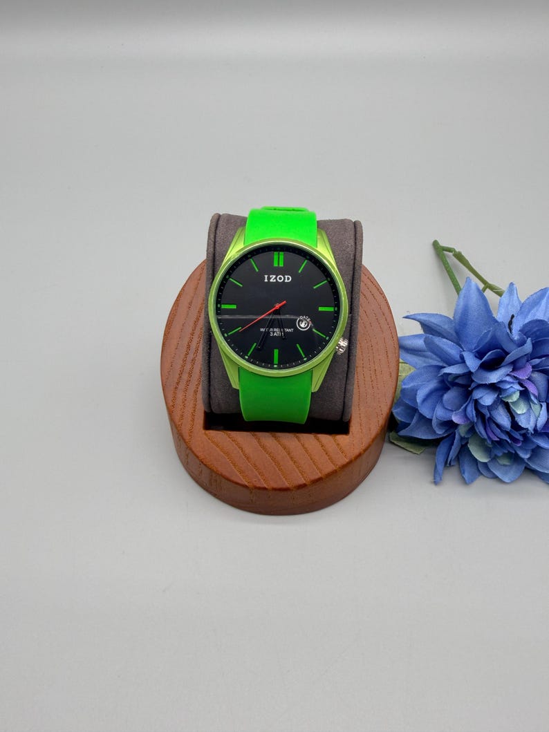 May include: An Izod wristwatch featuring a bright lime green silicone strap and matching lime green case. The watch face is black with lime green hour markers, a red second hand, and a small date window at the four o'clock position.