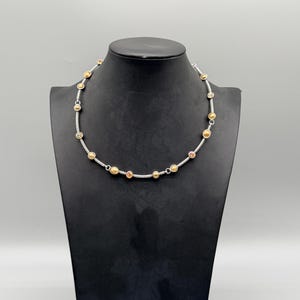May include: A necklace featuring a twisted silver-tone metal chain interspersed with small, round, gold-tone metal beads and circular accents. The design includes evenly spaced metallic elements along the entire length of the cable-style chain.