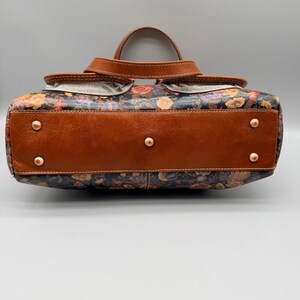 May include: A floral print handbag with brown leather accents. The bag features a top handle and a brown leather base with copper rivets. The floral pattern includes red, orange, and yellow flowers on a dark background.