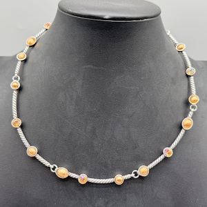 May include: A silver-toned necklace featuring a twisted cable chain design. The chain is accented with evenly spaced, round, amber-colored cabochon stones and smaller, iridescent, multi-colored faceted crystals set in circular silver-toned metal bezels.