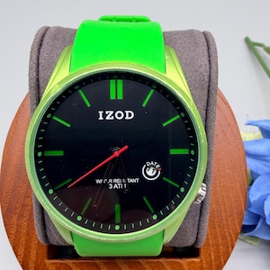 May include: An Izod wristwatch with a bright lime green silicone strap and matching bezel. The black dial features lime green hour markers, a red second hand, and a date window at the four o'clock position. The text reads IZOD and WATER RESISTANT 3 ATM.