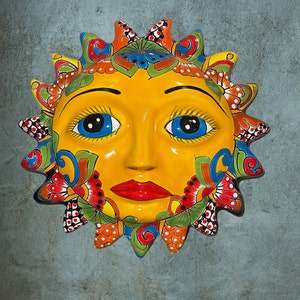 May include: A yellow ceramic sun with a smiling face, blue eyes, and red lips. The sun has a colorful floral design around the edges.