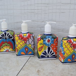 May include: Four ceramic soap dispensers with colorful floral patterns. The dispensers are white with blue, red, yellow, green, and orange accents. Each dispenser has a white pump.
