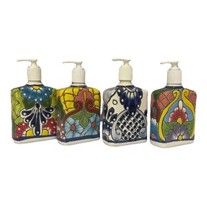 May include: Four ceramic soap dispensers with colorful floral designs. Each dispenser has a white pump and a square base. The designs feature a variety of colors, including blue, green, yellow, red, and pink.
