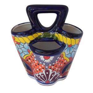 May include: A colourful ceramic utensil holder with three compartments and a handle. The holder is decorated with a floral pattern in shades of blue, yellow, orange, and green.