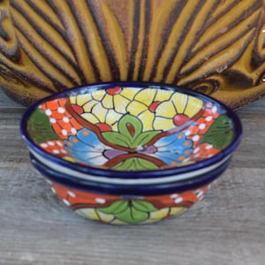 May include: A set of three small, colorful ceramic bowls with a floral design. The bowls are stacked on top of each other and have a blue rim.
