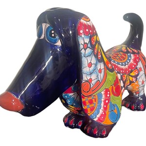 May include: A hand-painted ceramic dog figurine with a blue base and colorful floral patterns. The dog has a long snout and floppy ears.