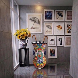 May include: A colorful ceramic umbrella stand with a floral design, holding two umbrellas with curved handles. A vase of sunflowers sits on a black stand. Framed umbrella art decorates the wall.