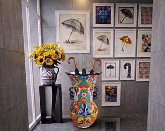 May include: A vibrant ceramic umbrella stand with a floral pattern, containing two umbrellas with curved handles. A vase of sunflowers sits on a black stand. Framed umbrella art decorates the wall.