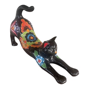 May include: Black ceramic cat figurine with colorful floral designs painted on its back and tail. The cat is in a stretched out pose with its head turned to the side.