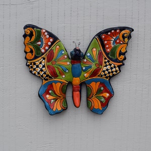 May include: A colorful ceramic butterfly wall decor with intricate patterns in shades of blue, green, red, yellow, and black. The butterfly has a detailed design with floral and geometric motifs.