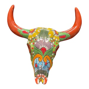 May include: A colorful ceramic bull skull with orange horns and a floral design in shades of green, yellow, blue, and purple.